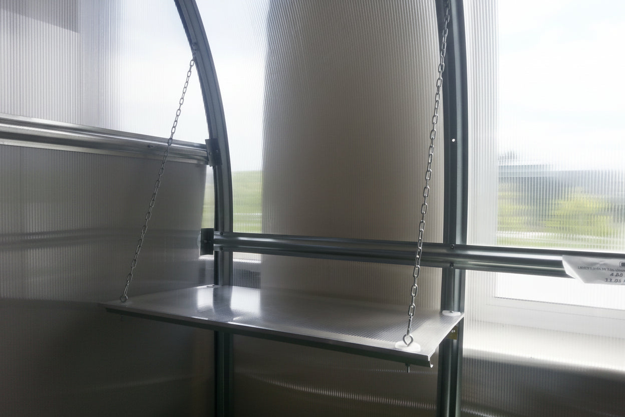 Steel greenhouse shelf suspended by chains from horizontal bar inside arc
polycarbonate greenhouse — interior staging accessory with chain and tube
support system Ireland